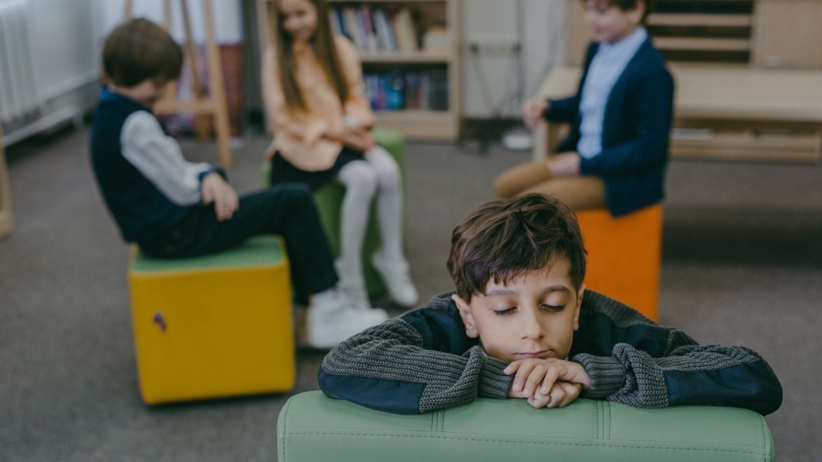 Enfant isolé en classe pendant qu’un groupe discute à l’arrière-plan, illustrant le harcèlement scolaire et l’importance de développer l’empathie dès le plus jeune âge.