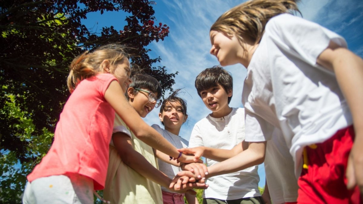 Groupe d’enfants jouant ensemble en cercle à l’extérieur, se tenant les mains avec enthousiasme, illustrant la coopération, l’inclusion et le jeu collectif.